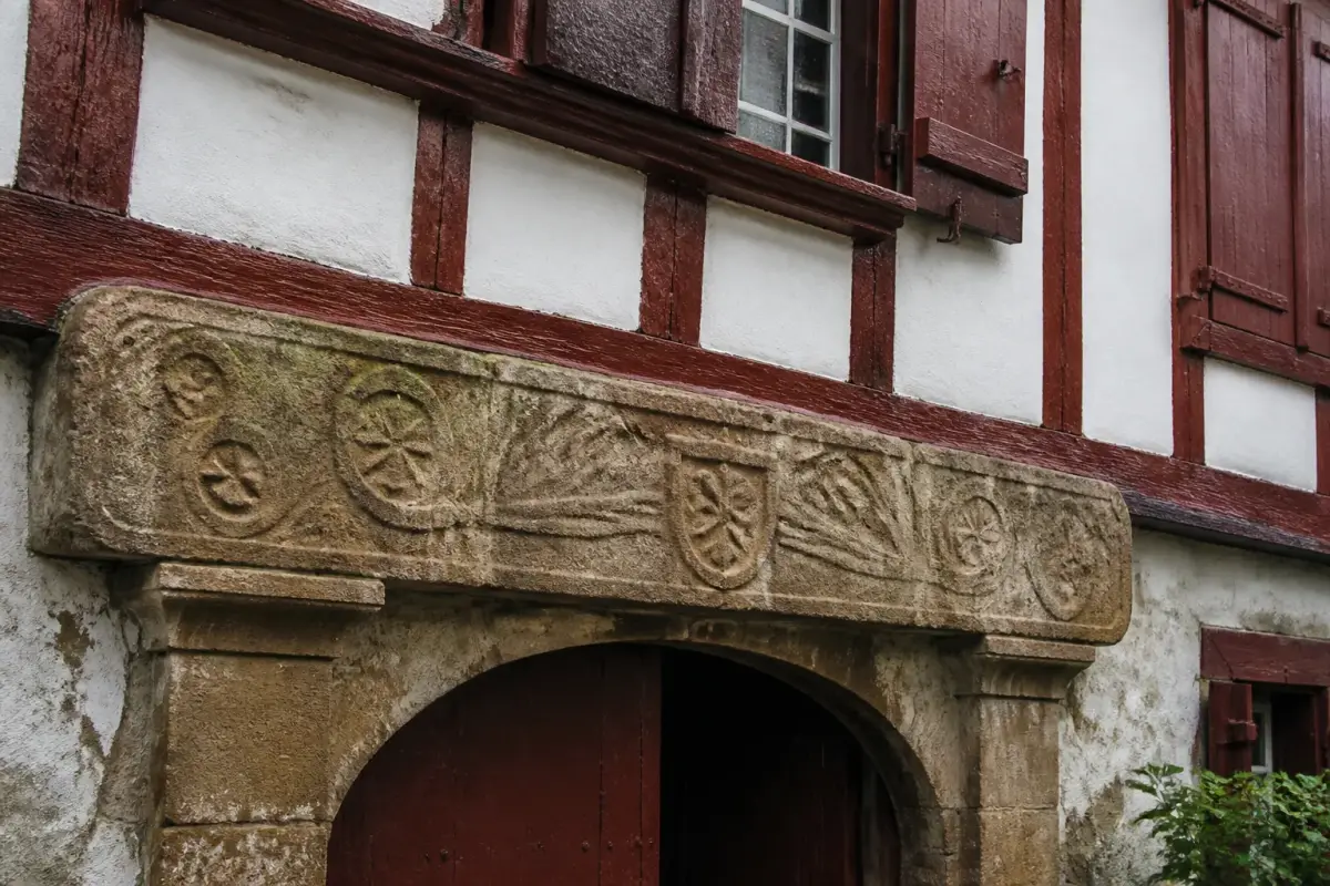 Linteau de pierre sculpté au-dessus de la porte cintrée d'une ferme basque aux colombages rouges.
