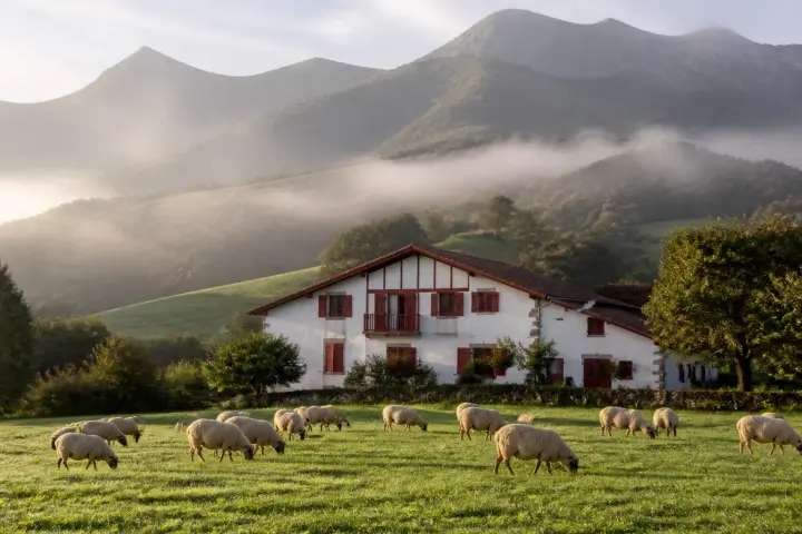 Village basque aux maisons blanches à colombages rouges, au pied de la Rhune, sous un ciel de traîne.