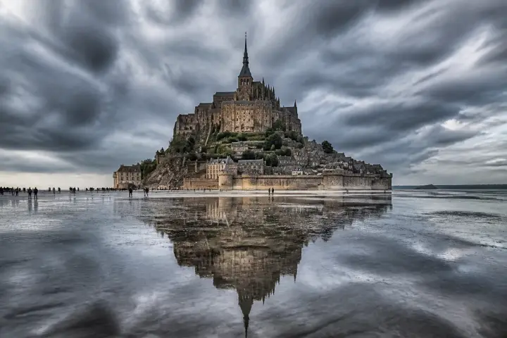 Le Mont-Saint-Michel et sa flèche dorée émergeant de la baie à marée haute, sous une lumière rasante.