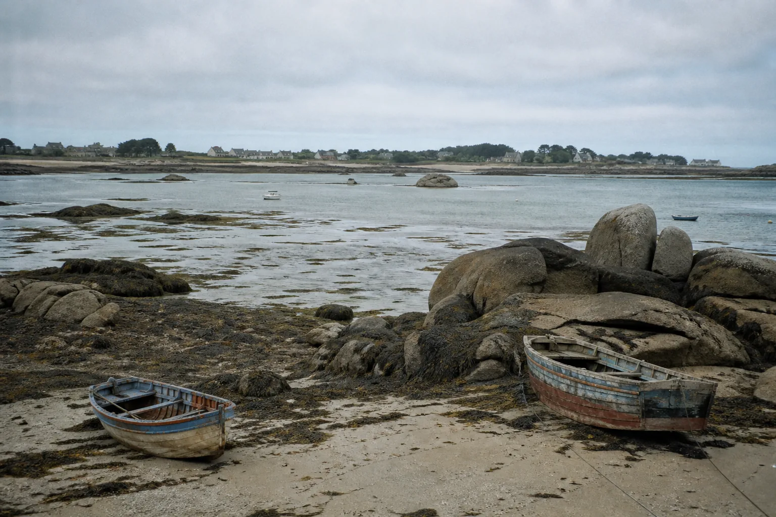Chapelle de granit isolée sur la côte du Finistère, avec un calvaire et la mer grise en arrière-plan.
