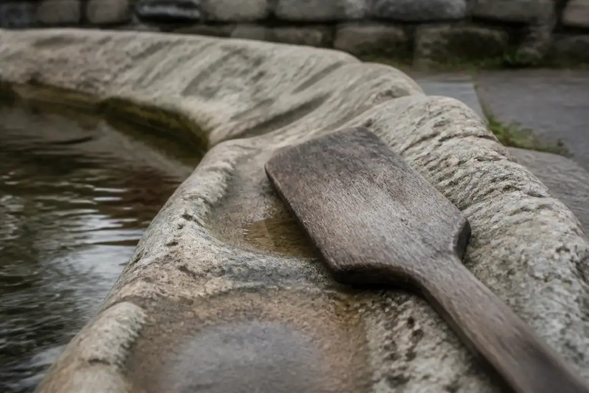 Margelle de pierre usée d'un lavoir avec un battoir de bois posé sur le rebord.
