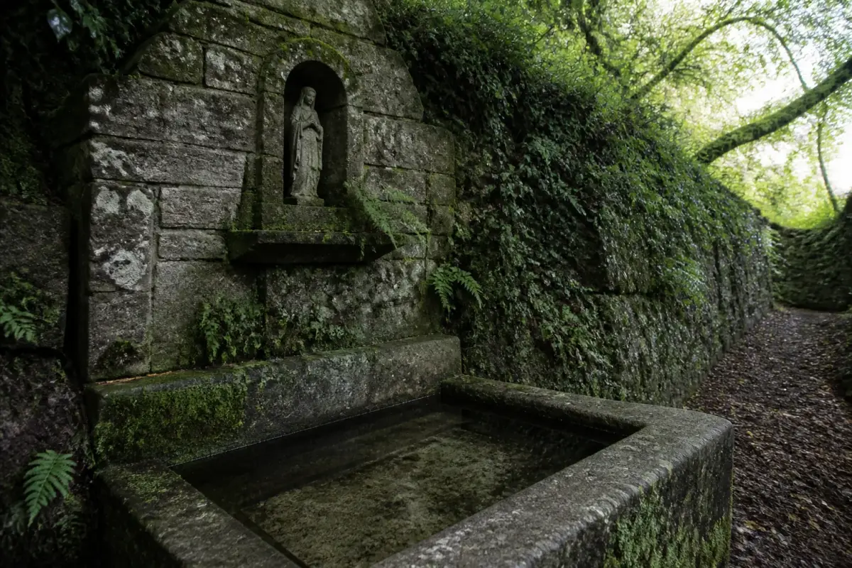 Une fontaine de dévotion en granit nichée dans un talus moussu au bord d'un chemin breton.