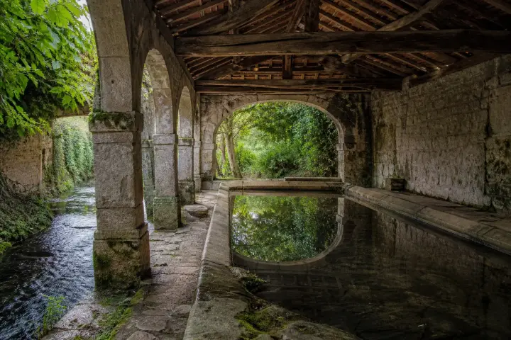 Lavoir couvert au toit de tuiles ouvert sur un bassin d'eau claire, entouré de pierres usées, dans un village de Bourgogne.