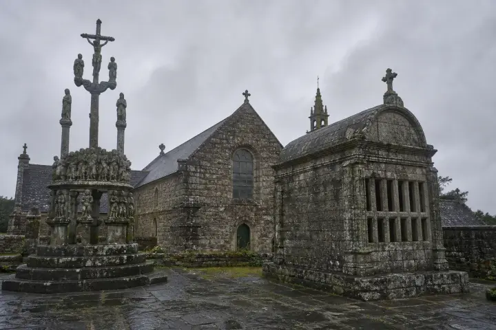 Groupe de marcheurs suivant un chemin creux bordé de talus fleuris en direction d'une cathédrale bretonne.